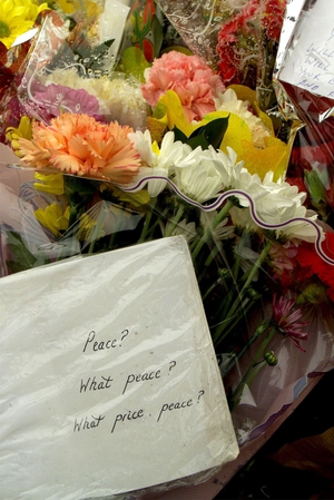 Flowers and cards are laid at the scene of blast, with one reading 'Peace? What peace? What price, peace?'