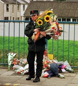 A RUC officer carries flowers left for victims of the blast