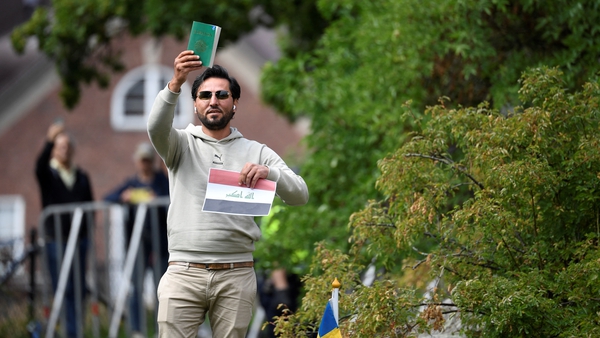 Salwan Momika holds up the Muslim holy book and a sheet of paper showing the flag of Iraq during a protest outside the Iraqi Embassy in Stockholm, Sweden, in July