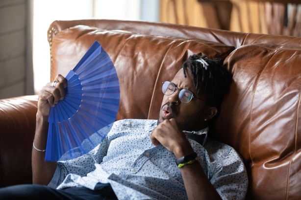 Man sitting at home on a sofa during heatwave, fanning himself 