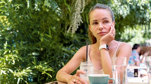 Woman sitting outdoors at a cafe on a hot day, looking down and tired