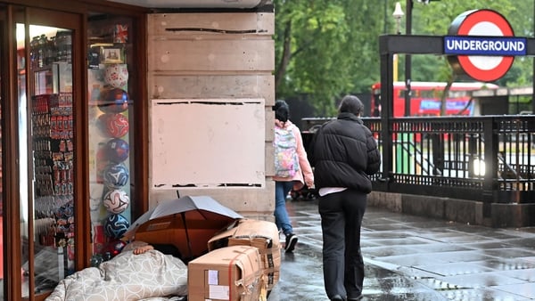 A pedestrian walks in the rain past a rough sleeper outside a closed shop on Oxford Street in London