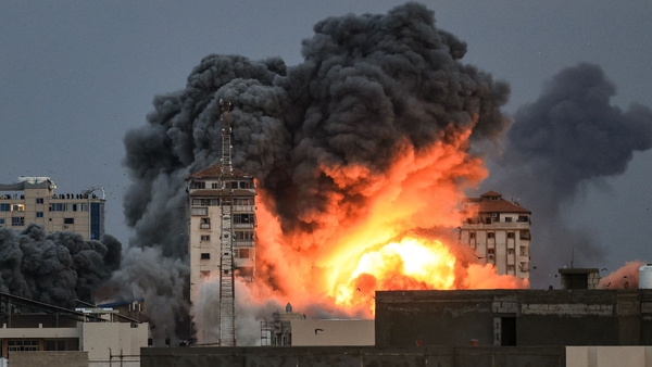 People standing on a rooftop watch as a ball of fire and smoke rises above a building in Gaza