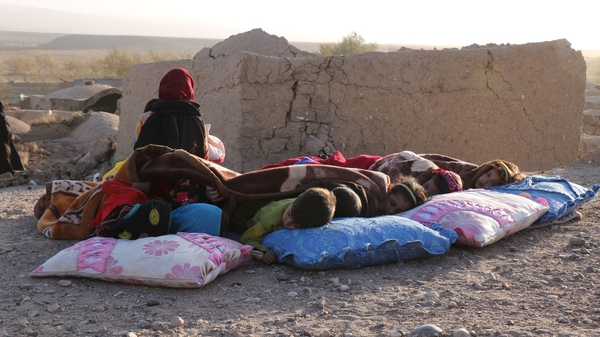 Children rest beside damaged houses after an earthquake in Sarbuland village