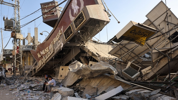 A Palestinian man and his son sit holding a bag of bread outside a destroyed bakery at the Nuseirat refugee camp in the central Gaza Strip
