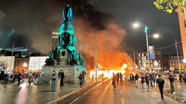 A bus is on fire on Dublin's O'Connell Street during a night of unrest in the city centre. The unrest started following a knife attack in which three children and a woman were injured. A Luas tram was also set alight while some shops were looted.