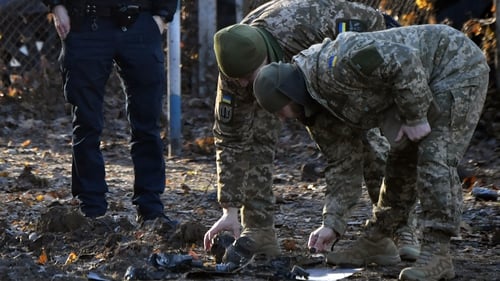 Ukrainian police and military experts collect fragments of downed Russian drone near a crater in a yard amid residential buildings in Kyiv