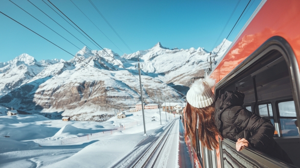 Happy woman traveler looks out from window traveling by train in beautiful winter mountains, Travel 