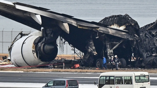 Officials look at the burnt wreckage of a Japan Airlines passenger plane on the tarmac at Tokyo International Airport
