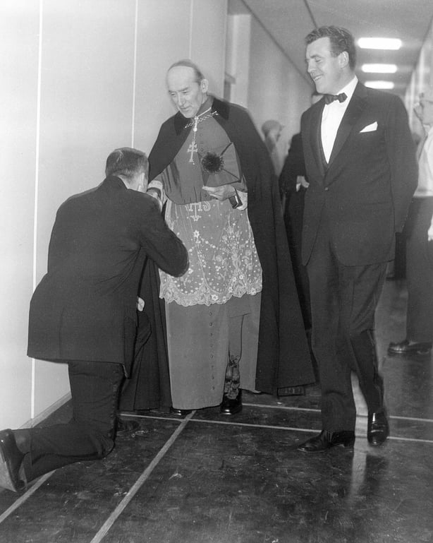 An unidentified man kisses the ring of the Roman Catholic Archbishop of Dublin John Charles McQuaid, in the Television Centre building at RTÉ's Montrose campus in Donnybrook, Dublin, during Telefís Éireann's opening night on New Year's Eve 1961. Broadcaster Eamonn Andrews, then Chairman of Radio Éireann, is looking on. McQuaid gave the Benediction of the Blessed Sacrament from a studio at Montrose for this occasion