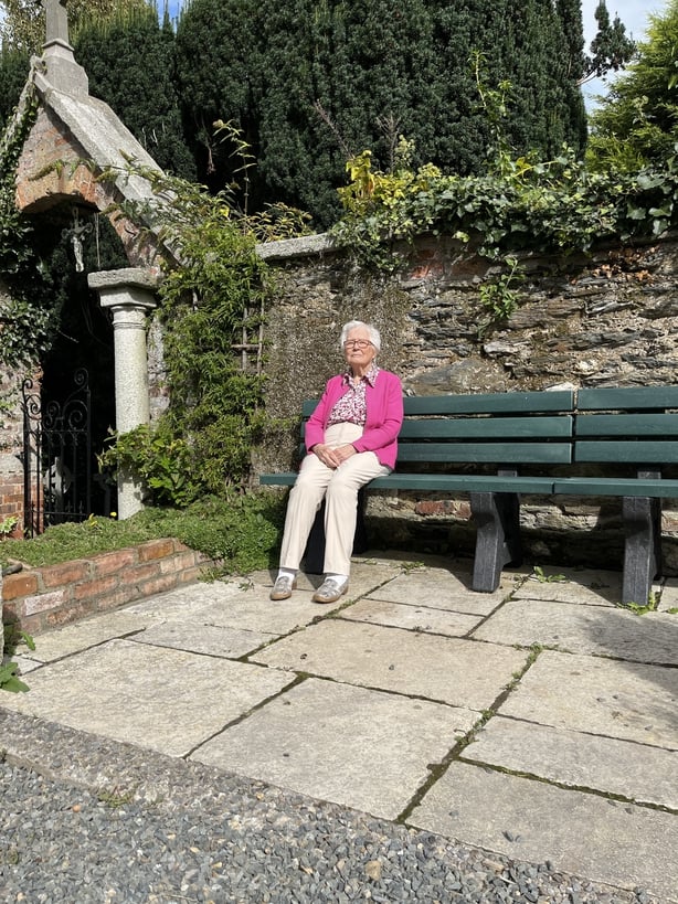 An older woman in a pink top sitting in a courtyard