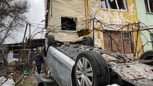 A man stands near debris and an overturned car at a residential building damaged by Russian shelling last week