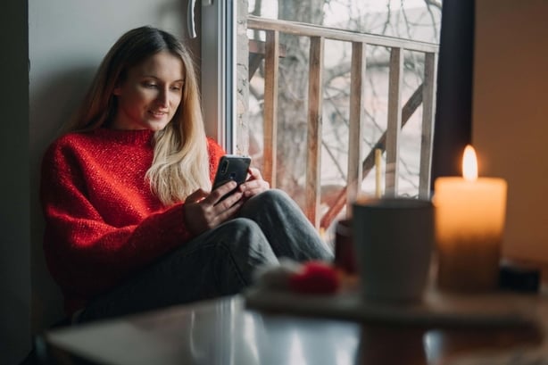 Woman sat with a phone in hand (Alamy/PA)
