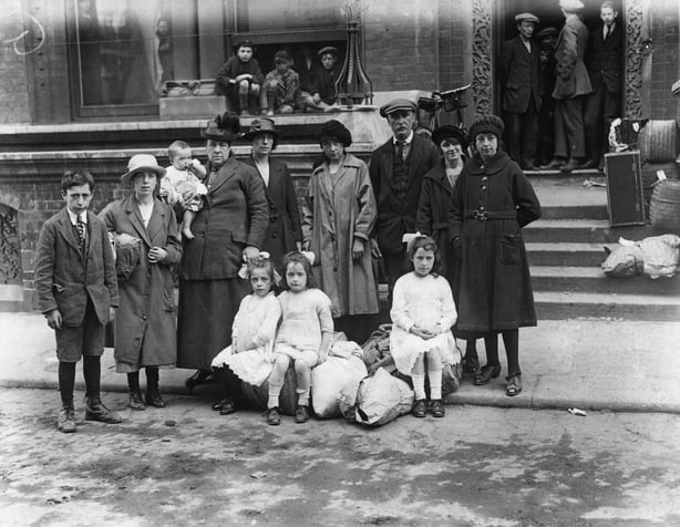Black and white photo showing a group of adults and children in 1920s clothes and baggage standing in the street in Dublin