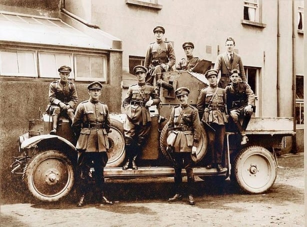 Sepia photo of soldiers standing around a car