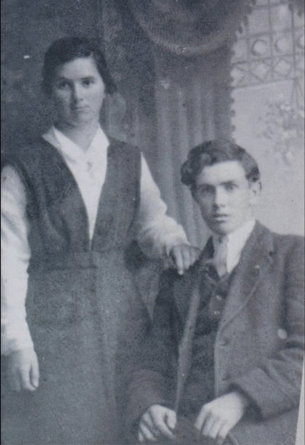 Black and white photo of a young man seated beside a standing young woman
