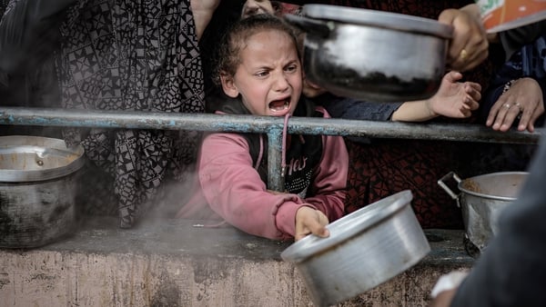 A child holds out a pot as she waits for food at a distribution centre in Rafah