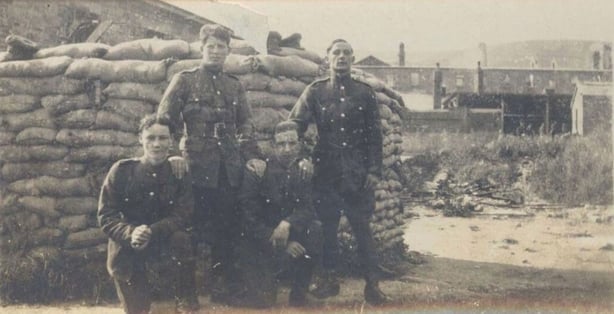 Young men in army uniform posing in front of sandbags
