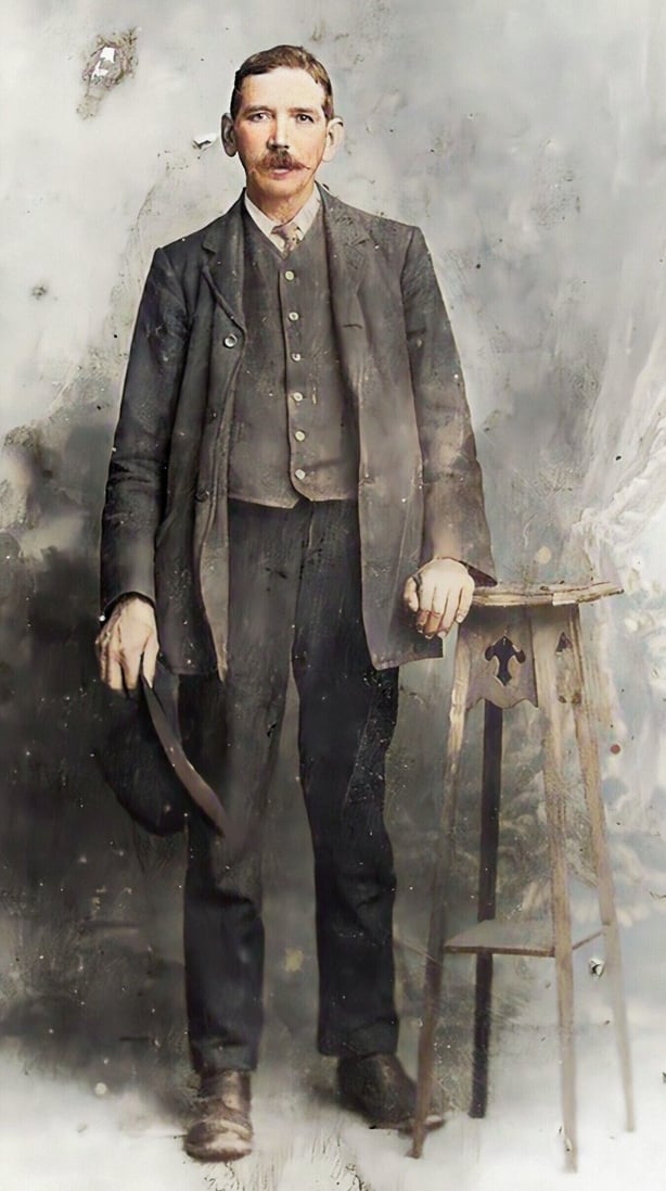 A colourised photo of a young man with a moustache wearing a suit