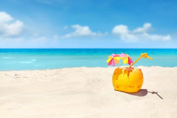 Coconut cocktail with straw and colorful umbrellas on a beach, summer holiday concept, selective focus, space for text.