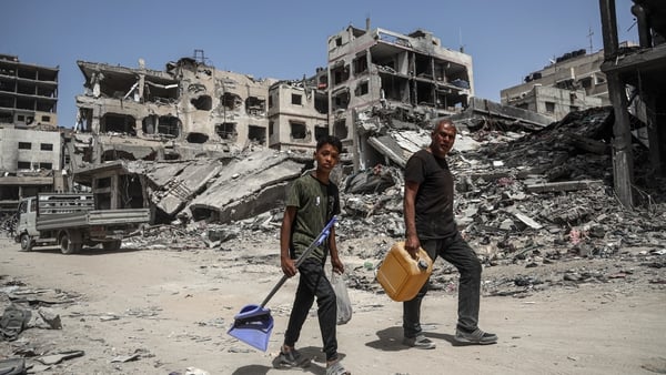People carrying cleaning supplies walk on a road lined with destroyed buildings and rubble in Khan Yunis in southern Gaza