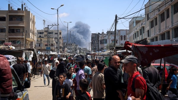 Palestinians crowd a street as smoke billows nearby from Israeli strikes in Rafah