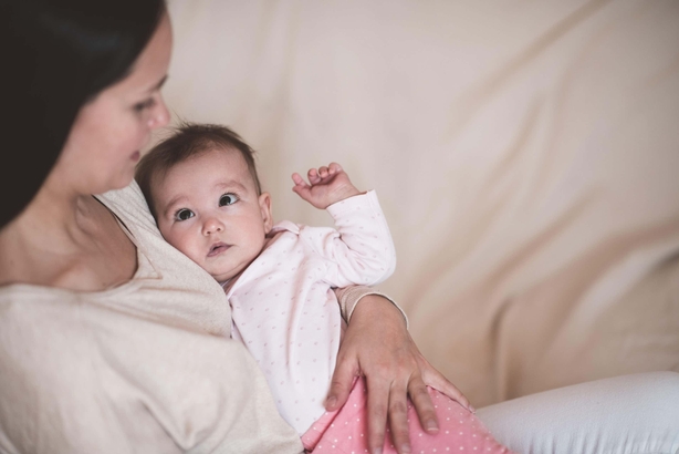 Woman holding baby wear pajamas lying on mother hand crying. Sad child girl have colics and stomach ache at home. Motherhood.