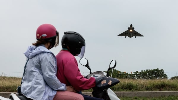 Two people ride a motorcycle as a Taiwanese Air Force Mirage 2000 fighter jet approaches for landing at an air force base in Hsinchu in northern Taiwan
