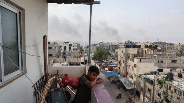 A boy stands on a balcony with a view of billowing smoke due to renewed Israeli strikes in Rafah city