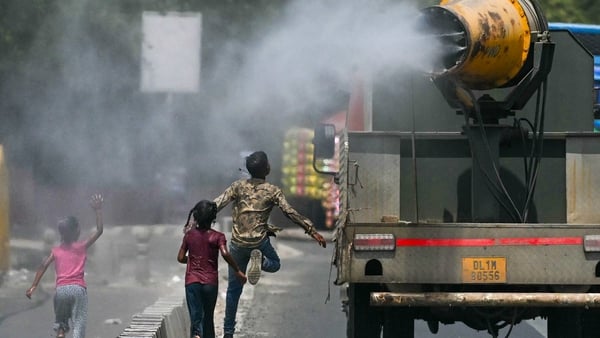 Children run behind a truck spraying water along a street in New Delhi amid record temperatures