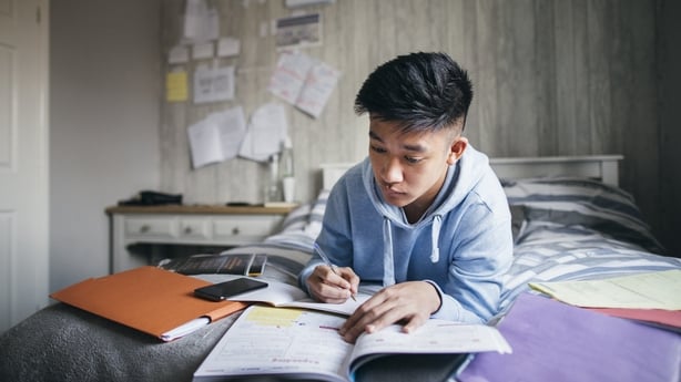 Teenage boy lying on his bed while concentrating on homework for his exams