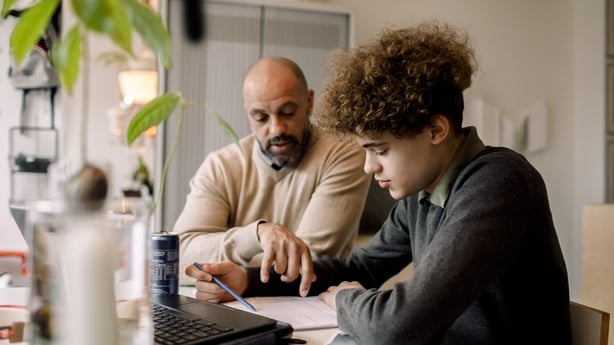 ather guiding son doing homework while sitting at table