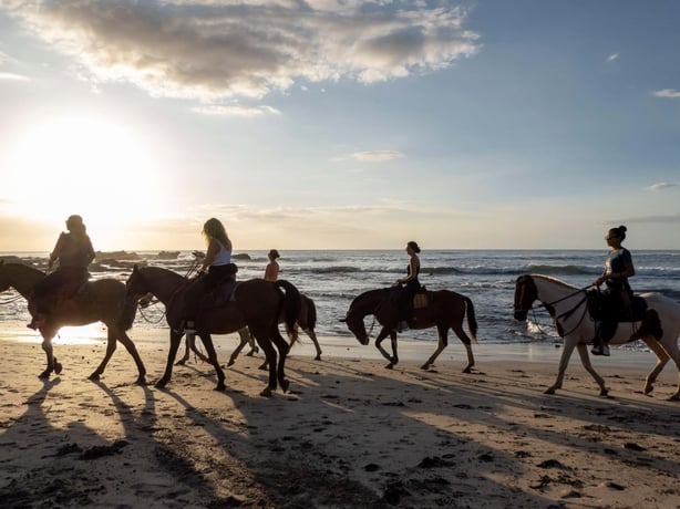 A group of horse riders enjoy time on the beach as the sun starts to set in Nosara in Costa Rica