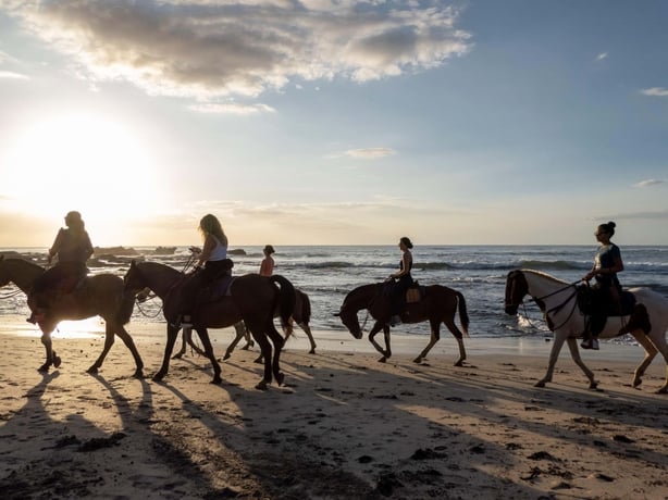 A group of horse riders enjoy time on the beach as the sun starts to set in Nosara in Costa Rica