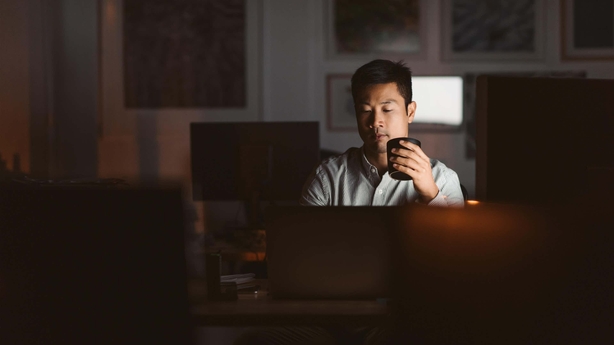 Young Asian businessman working at his desk in an office late at night drinking a cup of coffee to stay awake