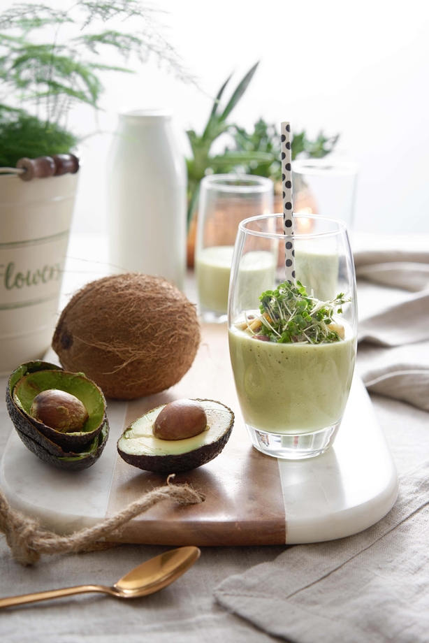 Green smoothie sits on kitchen counter next to avocados and a coconut