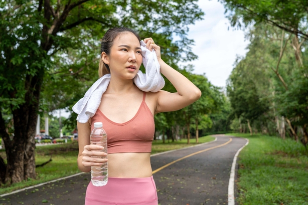 woman blots her face with a towel as she sweats during a workout