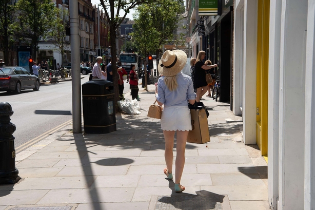 Woman walks down Chelsea high street in shorts and a big summer hat during heatwave