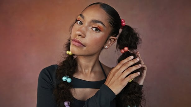 Portrait of teenage girl with hand in hair adjusting braids against brown backgroun