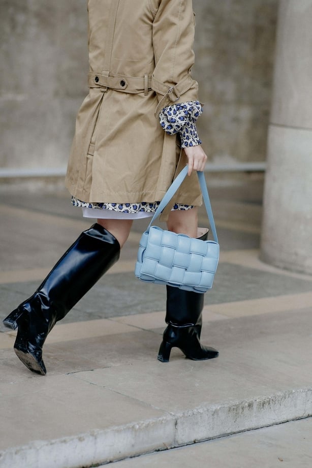 Woman walks through street in knee-high boots and skirt and trench