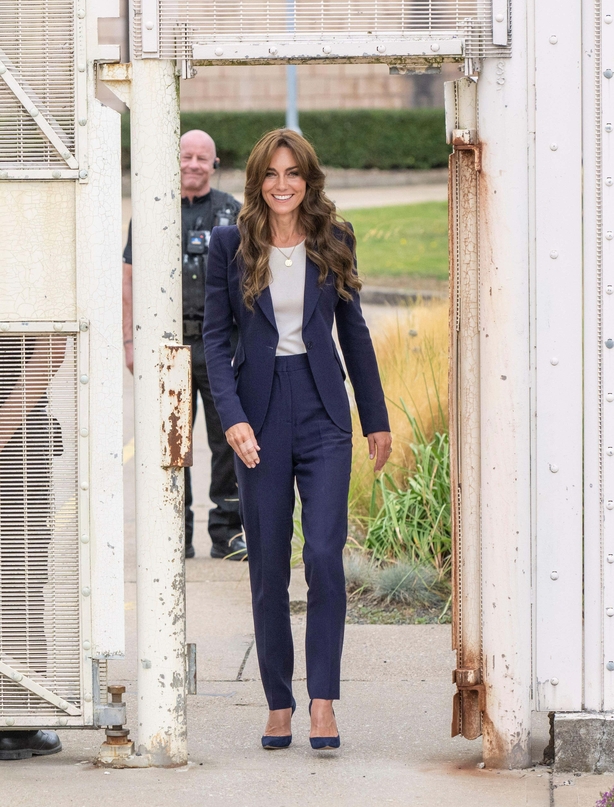 Kate walks through prison in navy blue suit with grey T-shirt and navy suede heels
