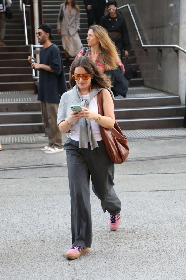 Woman walks across street in minimal trousers and top with pink trainers