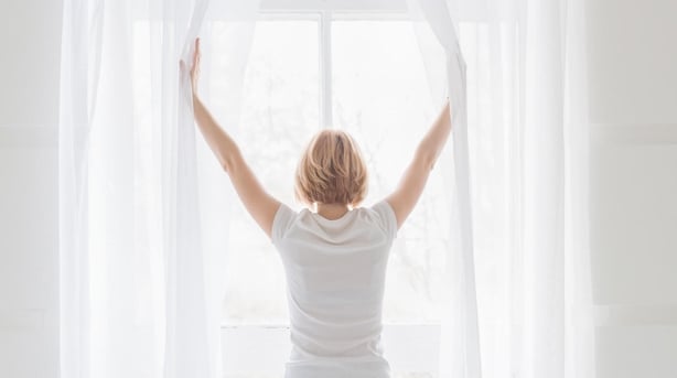 Young woman opening her bedroom curtains