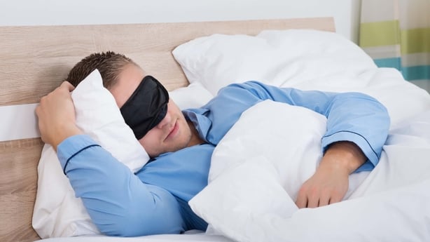 Young man wearing a blue shirt and a black eye mask sleeping in bed