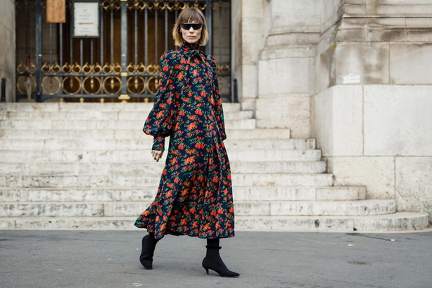 Woman walks through street in Stella McCartney red floral dress and black boots