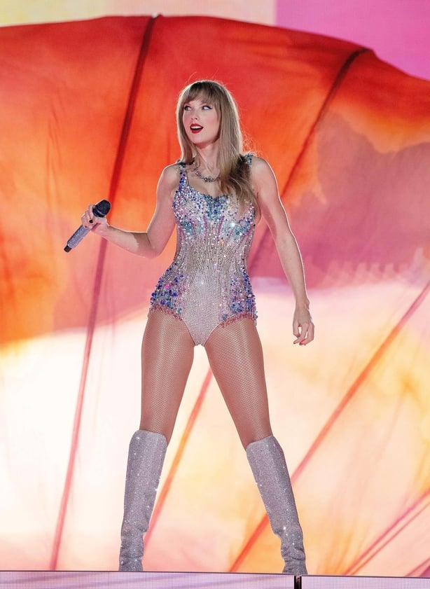 Taylor Swift poses on stage in sparkly playsuit