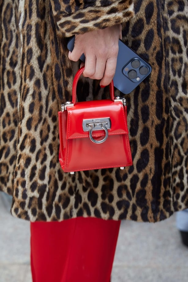 Woman in leopard print coat wears red tights and holds red bag
