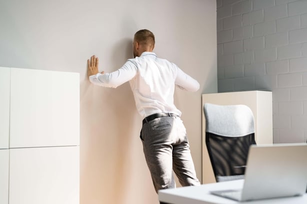 Man wearing a white shirt and grey suit trousers doing a push-up against a wall