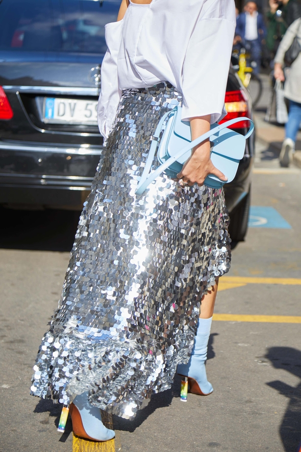 Woman with silver sequins skirt and pale blue bag and shirt walks through street