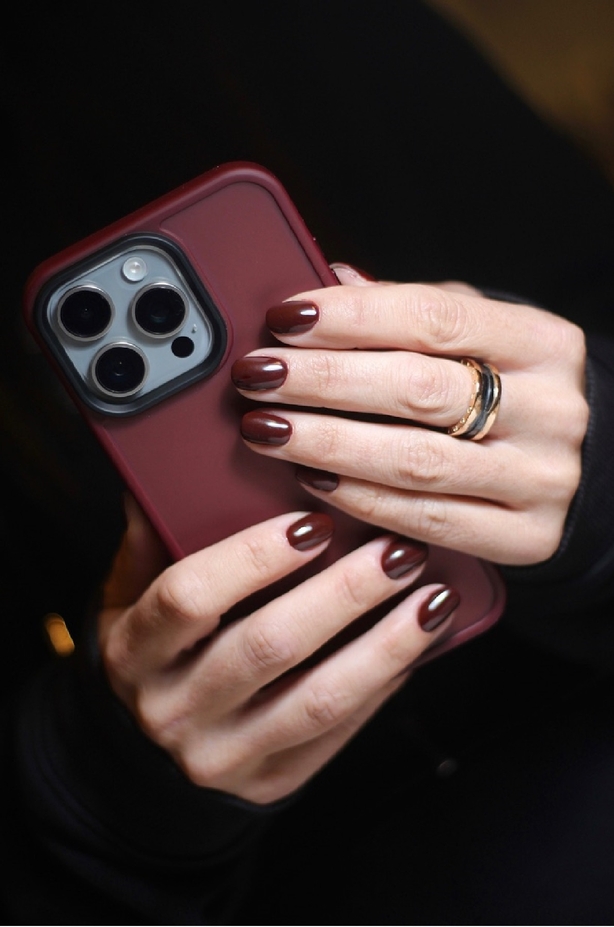 Woman with burgundy nails holds matching phone case